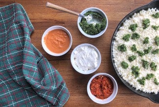 Pizza being topped with sauce, four bowls of sauce: pesto, romesco, white, and pink vodka.